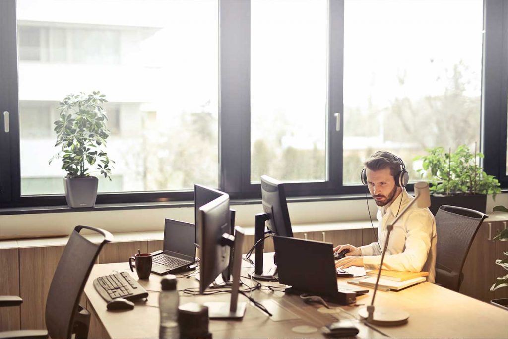 Male executive sitting in his office with several computers and wearing headphones