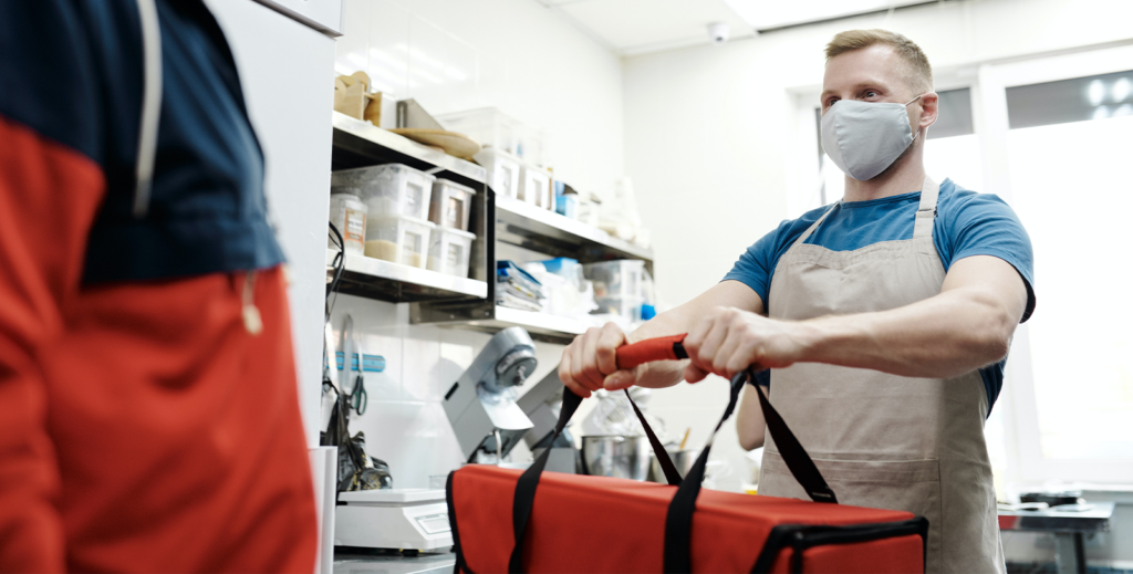 Male worker wearing a mask in a laboratory, accepting a delivery that is in a red and black bag